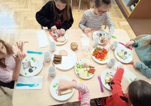 Siedzące dzieci przy stolikach komponują zdrowe kanapki
