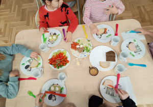 Siedzące dzieci przy stolikach komponują zdrowe kanapki
