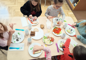 Siedzące dzieci przy stolikach komponują zdrowe kanapki