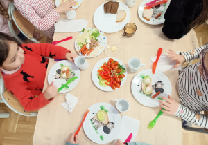 Siedzące dzieci przy stolikach komponują zdrowe kanapki