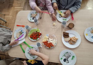 Siedzące dzieci przy stolikach komponują zdrowe kanapki