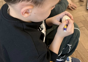 Chłopiec ozdabia drewniane jajko pastelami