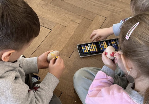 Dzieci ozdabiają drewniane jajka pastelami